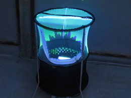 Photograph of the Gemlight Super LED light within a circular mesh enclosure, in a dark room lit by just the glow of the LED