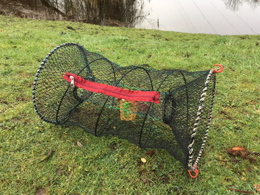 A photo of a portable crayfish trap resting on a river bank